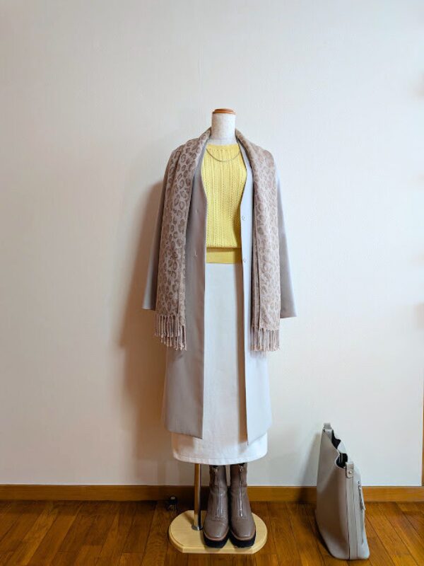 ライトイエローニットにホワイトライトスカート、ライトグレーコートを合わせたコーデ