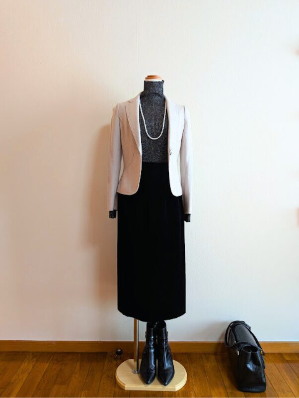 ブラックラメタートルニットにブラックベルベットスカート、ライトグレーのジャケットを合わせたコーデ