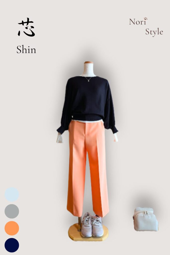 ホワイトシアーカットソーにネイビーのニットを重ね、オレンジのワイドパンツを合わせた芯コーデ。足元はライトグレーのスニーカー、そばにはライトミントのバッグを添え、静けさの中にまっすぐな軸とやわらかな光が共存する一枚。