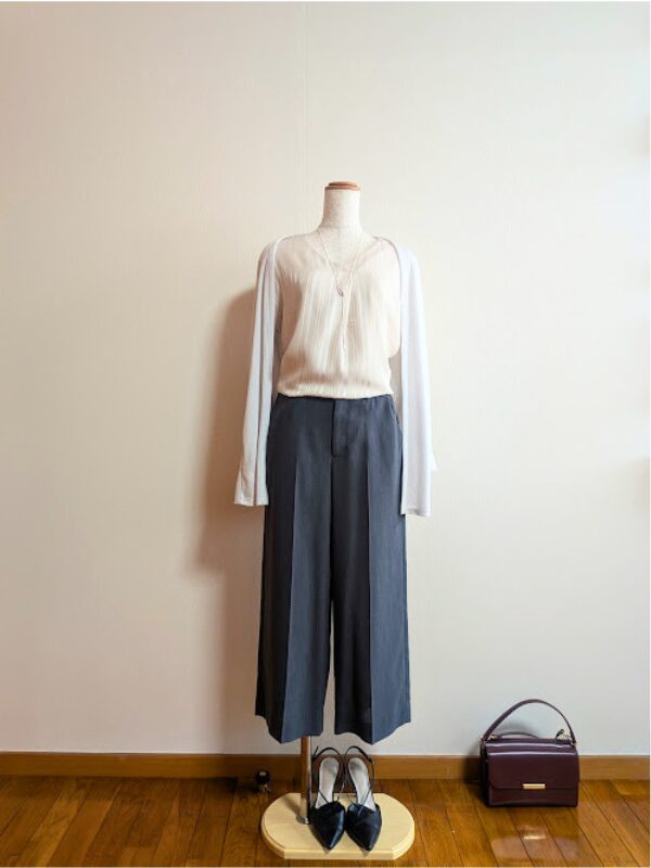 ピンクベージュのカットソーとダークグレーのセンタープレスワイドパンツ、その上からライトグレーのカーディガンを羽織ったトルソーのコーディネート。足元に黒いパンプス、右下にはボルドーのスクエアバッグが置かれている。