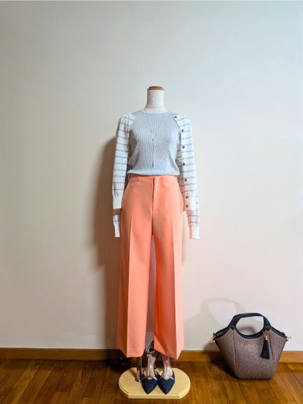 40代・50代大人の春夏きれいめコーデ。ライトグレーのフレンチスリーブニットにライトオレンジのワイドパンツ、ネイビーのボーダーカーディガンを肩掛けし、足元にネイビーのパンプス、ブラウンのかごバッグを合わせた上品なトルソースタイリング