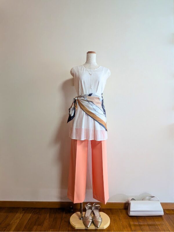 涼しげなホワイトのロングシアーブラウス(ロングシアー トップス)にポジティブなライトオレンジのワイドパンツを合わせ、ウエストに大判の柄スカーフをドラマチックに巻いた大人の最旬エレガントカジュアルコーディネート。